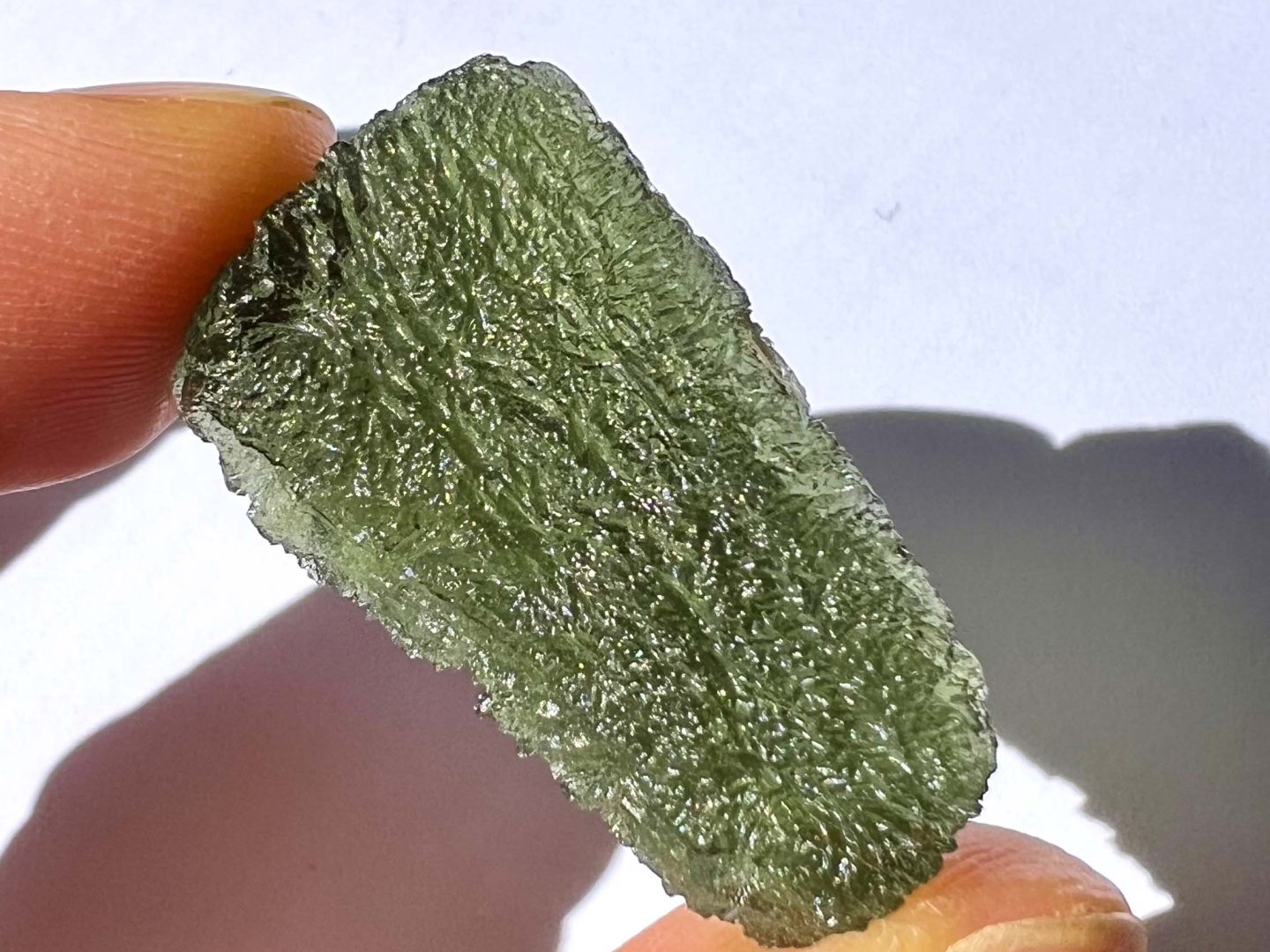 A genuine raw moldavite held between fingers in daylight